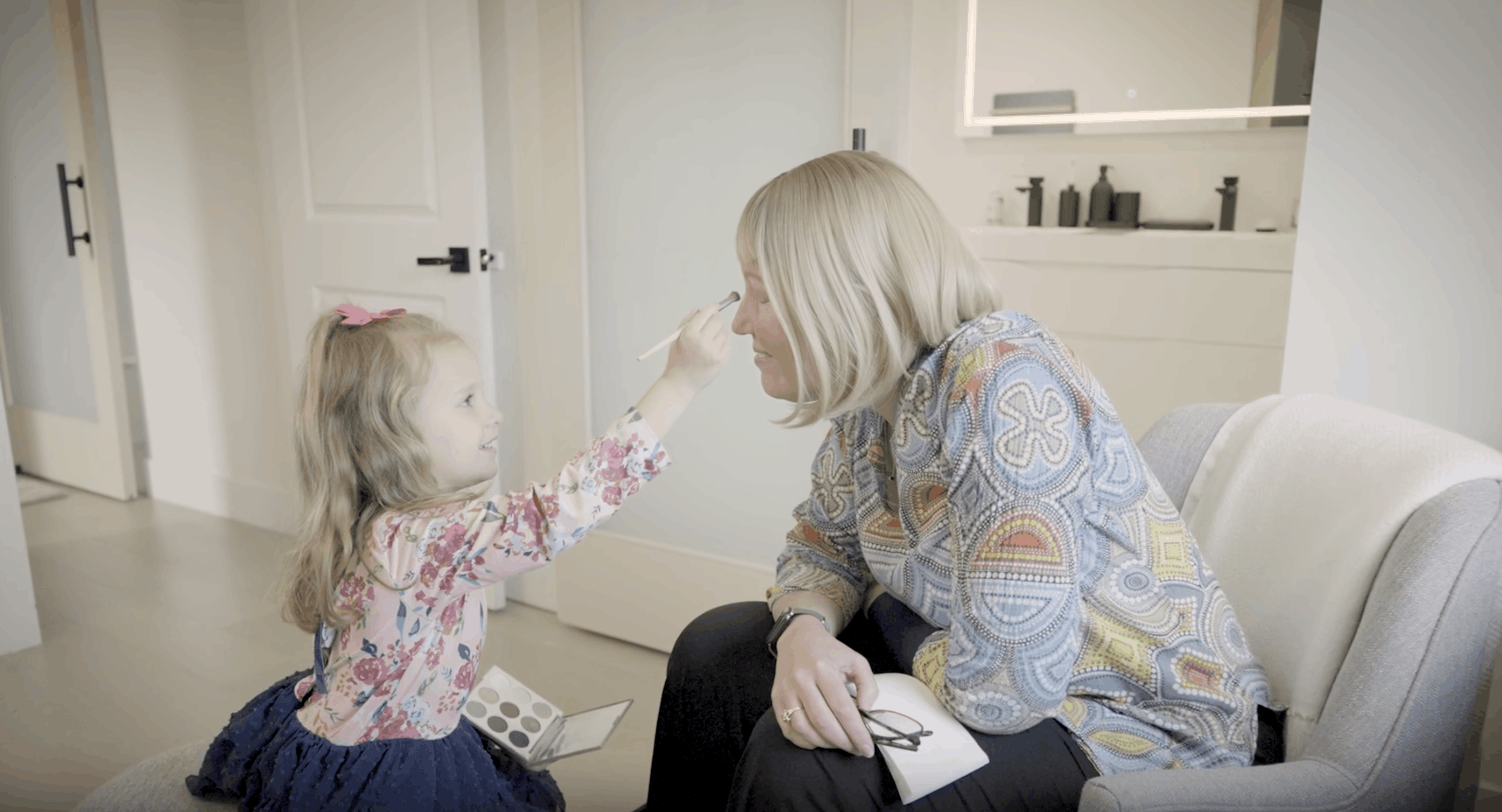 Esther sits with her granddaughter and lets her apply makeup to her face.