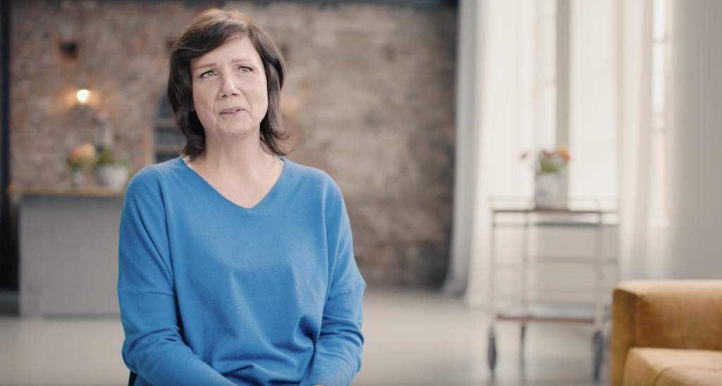 Katja sits in her living room in a blue sweater.