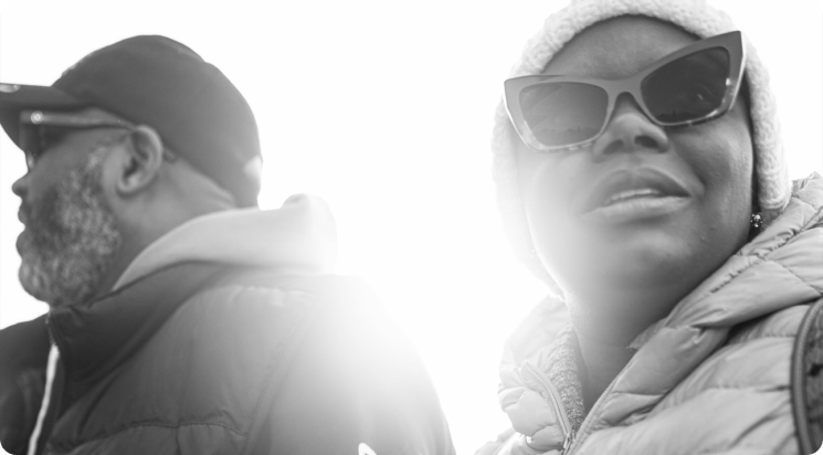 A black-and-white photograph of LaToya in sunglasses beside a man, both lit from the side.