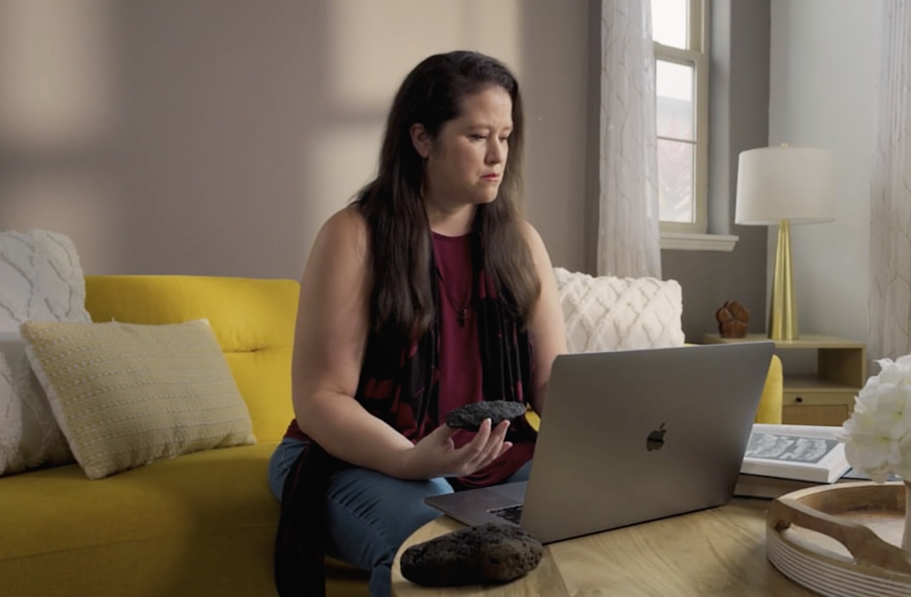 Melissa sits with a laptop on a yellow sofa by a window.