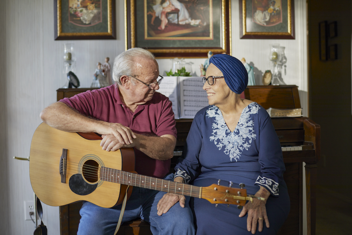 Joella and her husband sit next to and smile at each other.