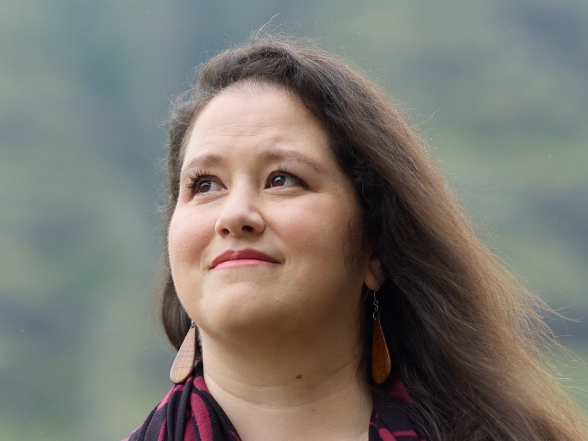 Melissa looks up and smiles, outdoors in soft light.