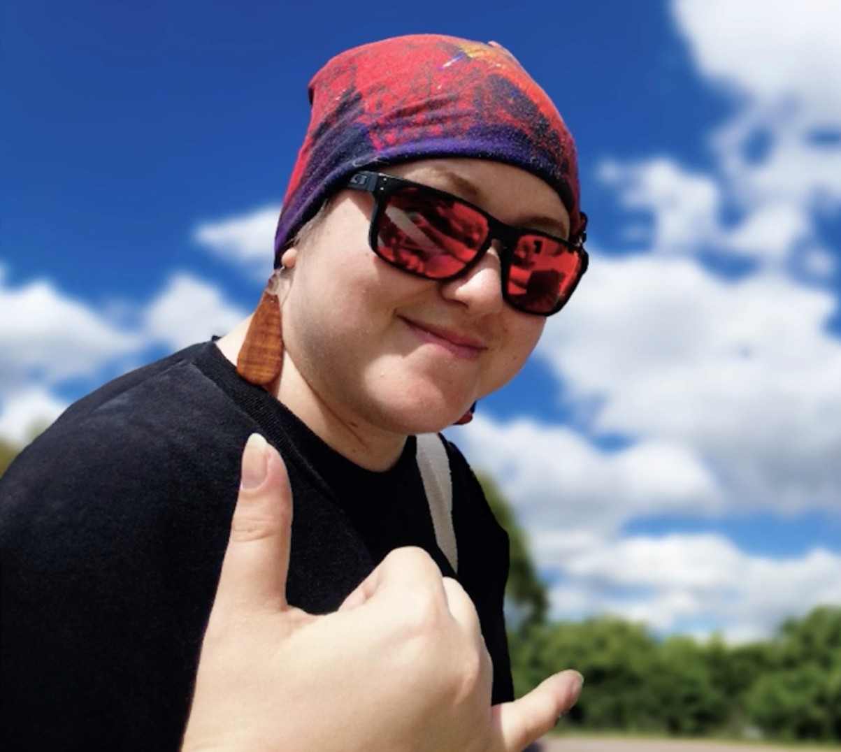 Melissa makes a shaka sign in sunglasses and a red headwrap against a blue sky.